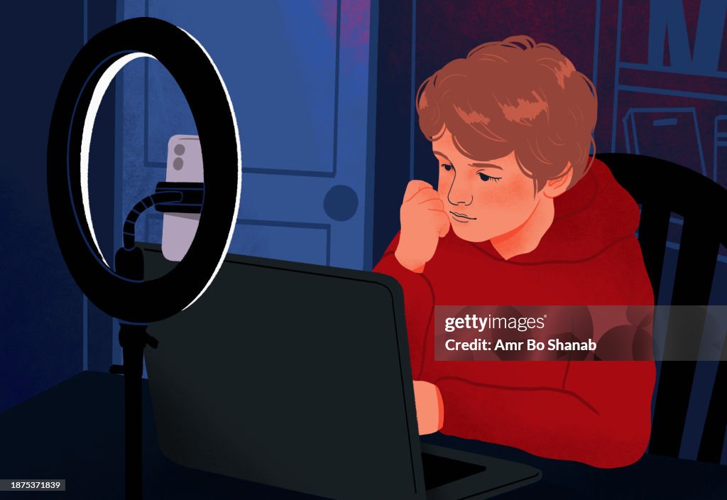 Boy using laptop in dark bedroom behind ring light and smart phone