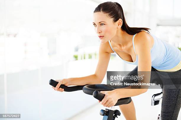 femme regardant loin tout en faisant de l'exercice sur vélo dans une salle de sport - cours de spinning photos et images de collection