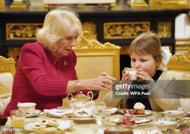Queen Camilla takes tea with seven-year-old Olivia Taylor from Sidcup at Windsor Castle, Berkshire on December 20, 2023 in Windsor, England. The...