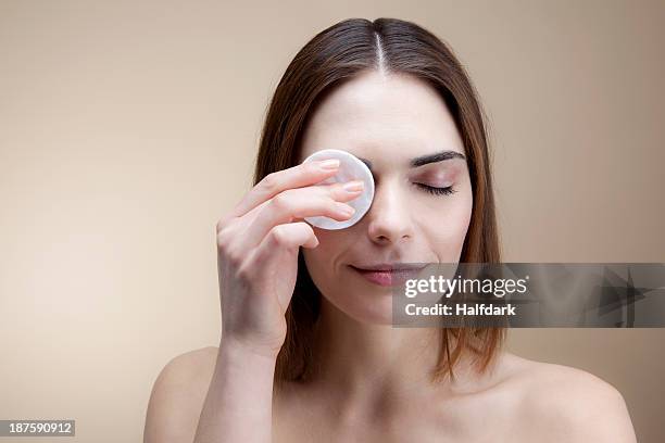 a smiling young woman using a cotton pad to clean her skin - wattepad stock-fotos und bilder