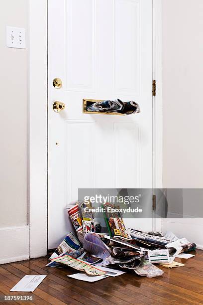 newspapers stuck in a mail slot above a heap of mail inside a front door - letterbox stockfoto's en -beelden