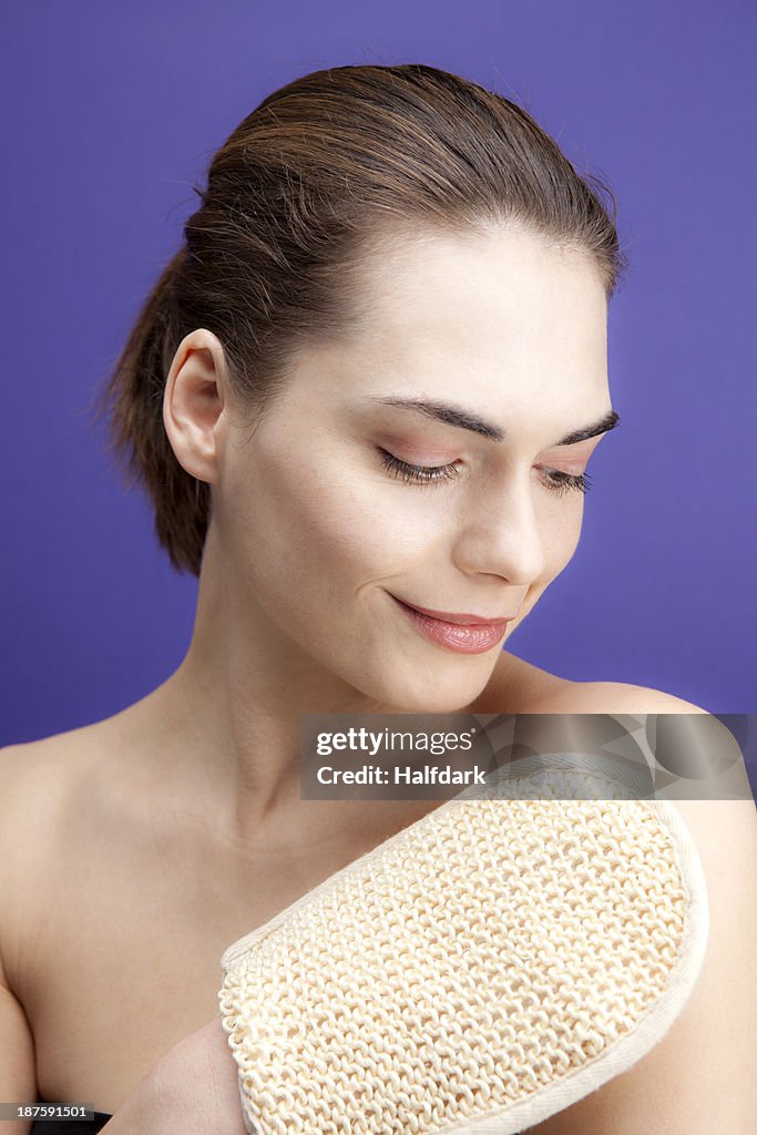 A smiling young woman using a loofah sponge