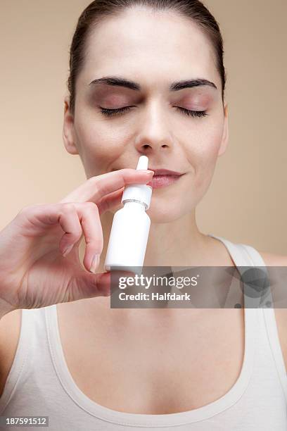 a serenely smiling young woman inhaling nasal spray - nasal spray stock pictures, royalty-free photos & images