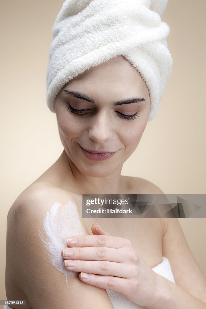 A smiling young woman applying lotion to her skin