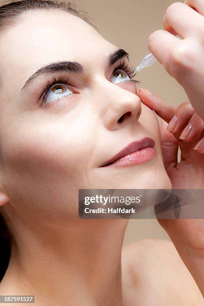 a serenely smiling young woman applying eye drops to her eyes - dry eye stock pictures, royalty-free photos & images