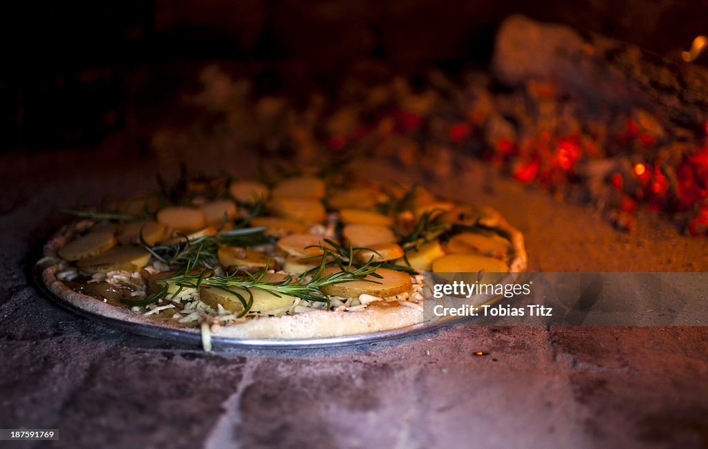 A rosemary and potato pizza baking in a brick pizza oven