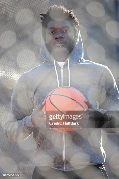 a hip young man holding a basketball and standing on an outdoor basketball court - chin piercing stock pictures, royalty-free photos & images