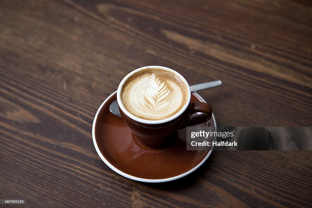 A cafe latte with a floral pattern in the milk froth on a table in a cafe
