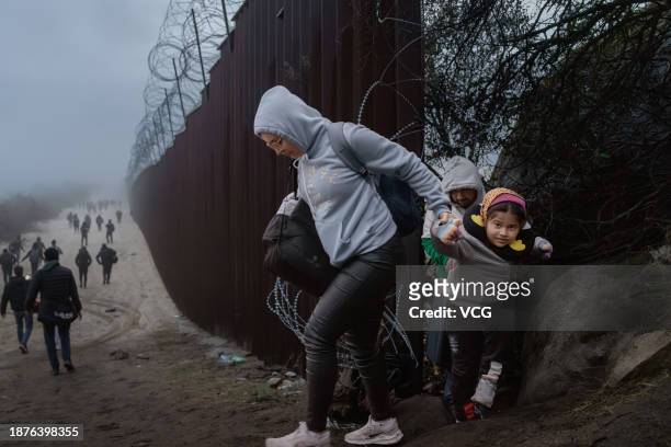 Migrants cross through a gap in the US-Mexico border fence on December 22, 2023 in Jacumba Hot Springs, California.