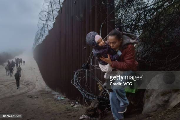 Migrants cross through a gap in the US-Mexico border fence on December 22, 2023 in Jacumba Hot Springs, California.
