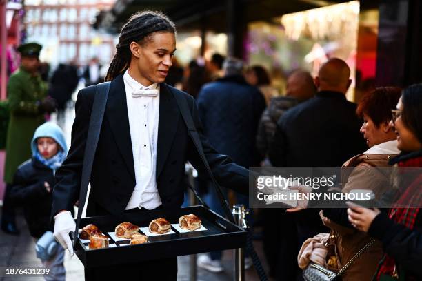 Member of staff distributes pastries to shoppers queueing to enter Harrods department store ahead of their Boxing Day sale, in central London, on...