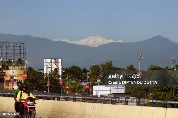 Indian commuters ride past as Mount Kangchenjunga is seen from Siliguri on November 11, 2013. Kangchenjunga is the world's third highest mountain at...