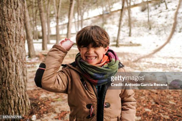 little boy throws snowballs at camera and smiles in a snowy forest - melting snowball stock pictures, royalty-free photos & images