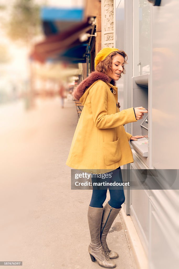 Young woman at ATM machine on street.