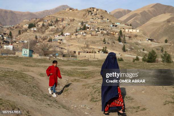 An Afghan burqa-clad woman with a girl, walks along a terrain in Fayzabad district of Badakhshan on December 26, 2023.