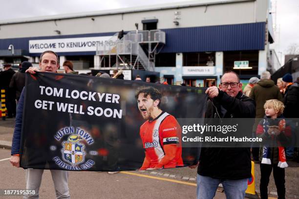 Fans pose for a photo whilst holding a banner displaying the message "Tom Lockyer get well soon" prior to the Premier League match between Luton Town...
