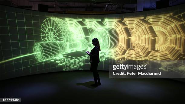 An employee of the Science Museum stands in front of a video projection showing the workings of the Large Hadron Collider at the 'Collider'...