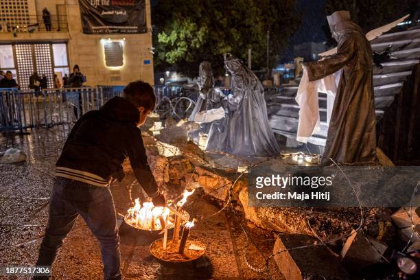 Boy lights a candle next to an art work "Nativity under the Rubble" by Palestinian artist Tariq Salsa in Manger Square near the Church of Nativity on...