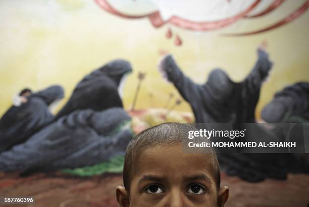 Bahraini Shiite Muslim boy poses in front of a painting depicting the story of Ashura, which commemorates the seventh century slaying of Imam...