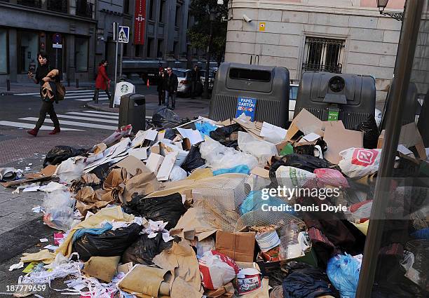 Woman walks past bins overflowing with rubbish in the city centre on November 12, 2013 in Madrid, Spain. Street cleaners, garbage collectors and...