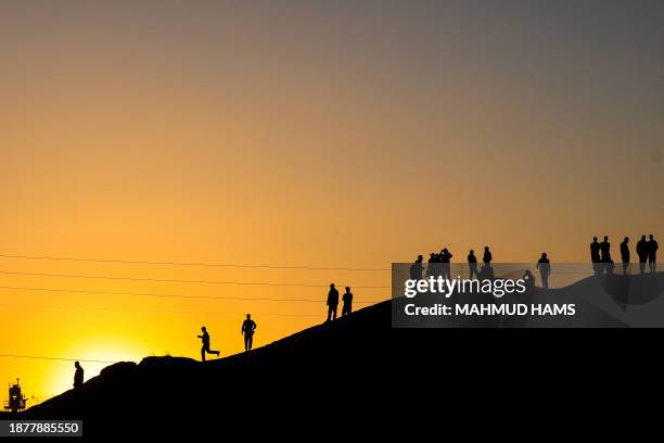 Palestinians are silhouetted against the setting sun as they stand on a hill on the Gaza-Egypt border in Rafah, on the southern Gaza Strip, on...