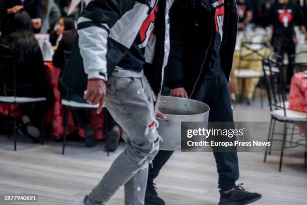 Two people carry a casserole during a charity dinner at Mirador de Cuatro Vientos, on 23 December, 2023 in Madrid, Spain. The solidarity initiative...