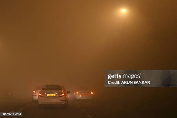 Vehicles travel through dense fog on a cold winter morning in New Delhi on December 27, 2023.
