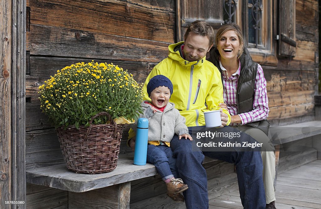 Happy young family sitting on bench, drinking tea