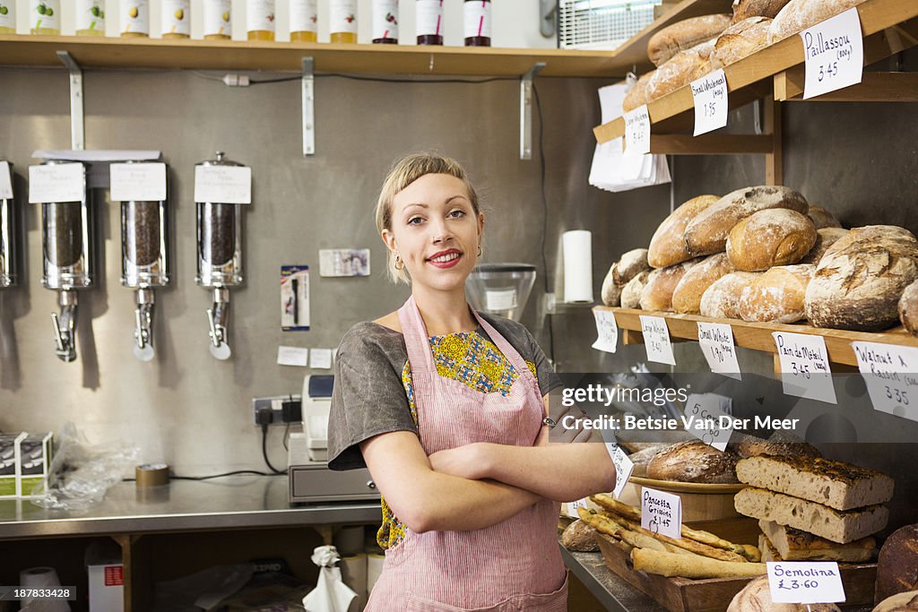 Shopkeeper in front of bread display in shop.