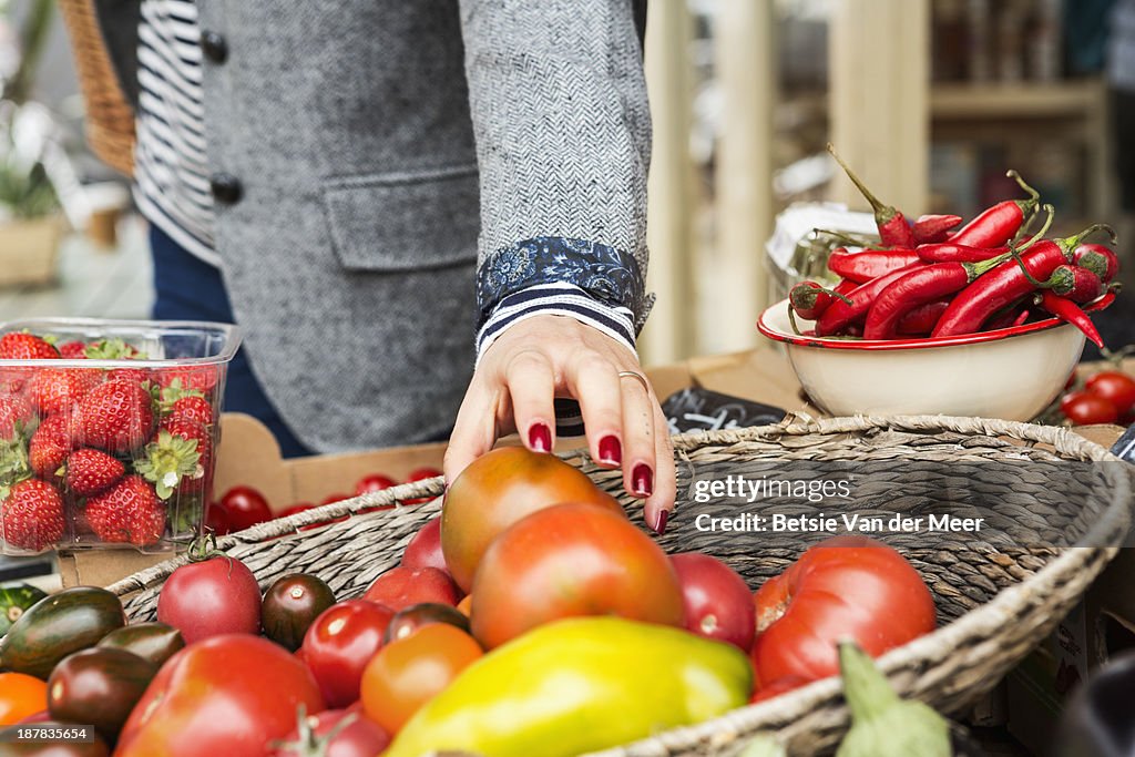 Close up of hand picking tomato from basket.