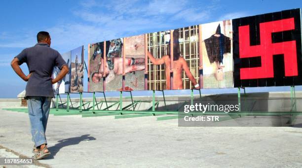 Cuban citizen walks past enormous posters of US soldiers torturing Iraqi prisoners at the Abu Ghraib prison. Posters are spread across the street in...