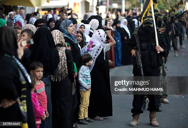 People look at members of the Palestinian Islamic Jihad movement parading with guns on November 13, 2013 in the streets of Gaza City during an...