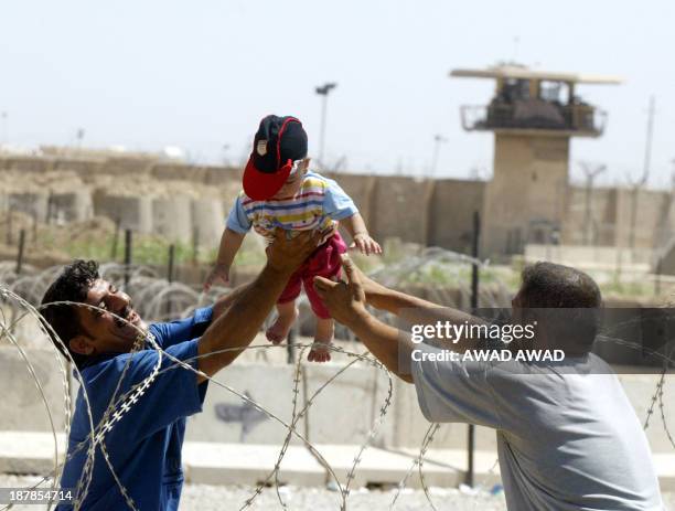 An Iraqi father reaches over barbed wire taking his son from an unidentified relative who brought the boy for a brief visit to see him as he takes...