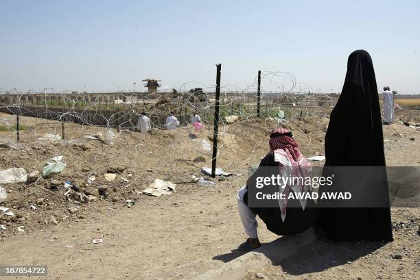 An Iraqi couple looks past the barbed wire at the notorious Abu Ghraib prison, west of Baghdad 04 June 2004, where a relative is being held. The past...