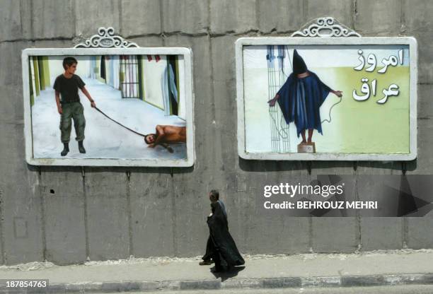 An Iranian couple walk past mural paintings depicting scenes from the torture of Iraqi prisoners by US soldiers at the Abu Ghraib prison near...