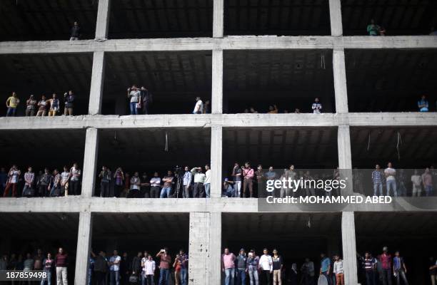 Palestinians standing on a building under construction look at security forces during an anti-Israel on November 13, 2013 in the streets of Gaza City...