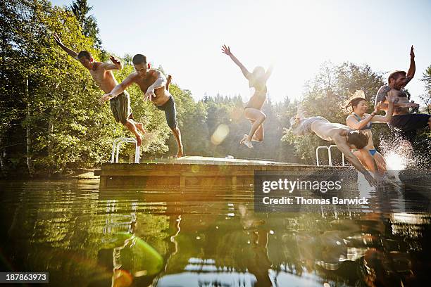 group of friends jumping off dock into lake - jumping into lake stock pictures, royalty-free photos & images