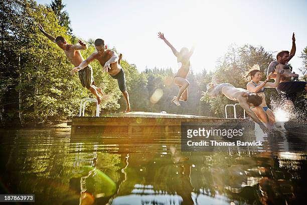 group of friends jumping off dock into lake - água parada imagens e fotografias de stock