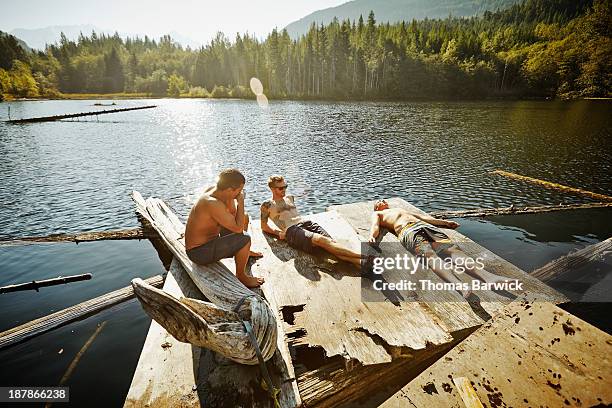 three friends relaxing in the sun on floating dock - schwimmende plattform stock-fotos und bilder