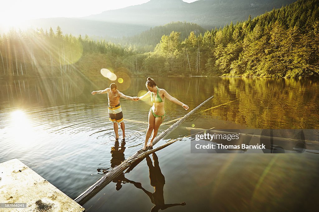 Couple balancing on logs in lake