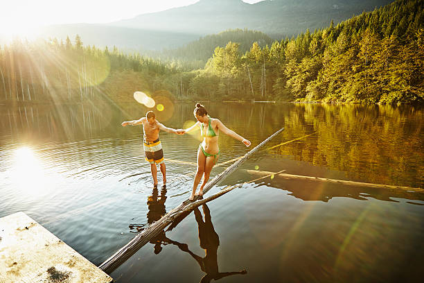 couple balancing on logs in lake - strong relationship couple stock pictures, royalty-free photos & images