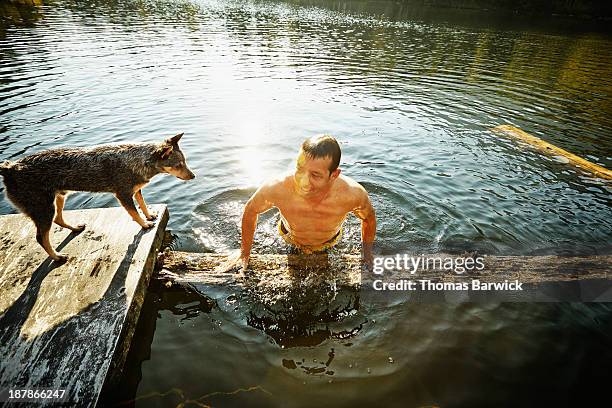 man pulling himself out of water onto log - dog swimming stock pictures, royalty-free photos & images