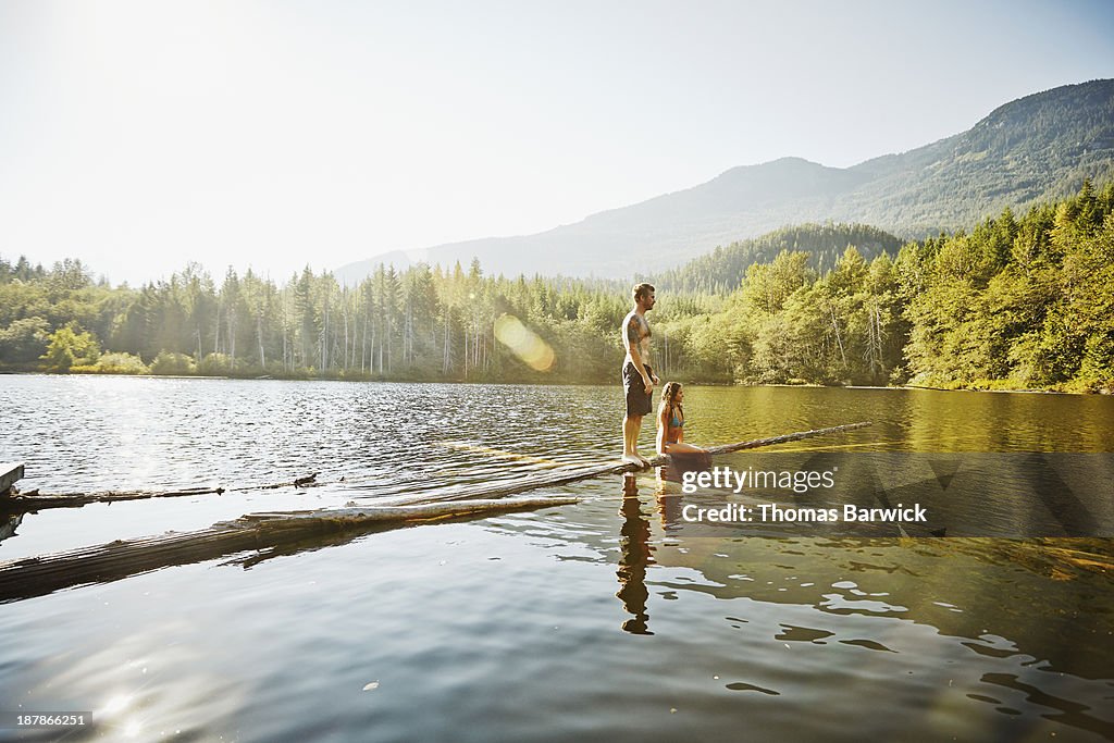 Woman sitting and man standing on logs in lake