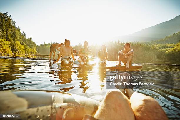 group of friends hanging out on floating dock - wasser und spaß und erwachsene stock-fotos und bilder