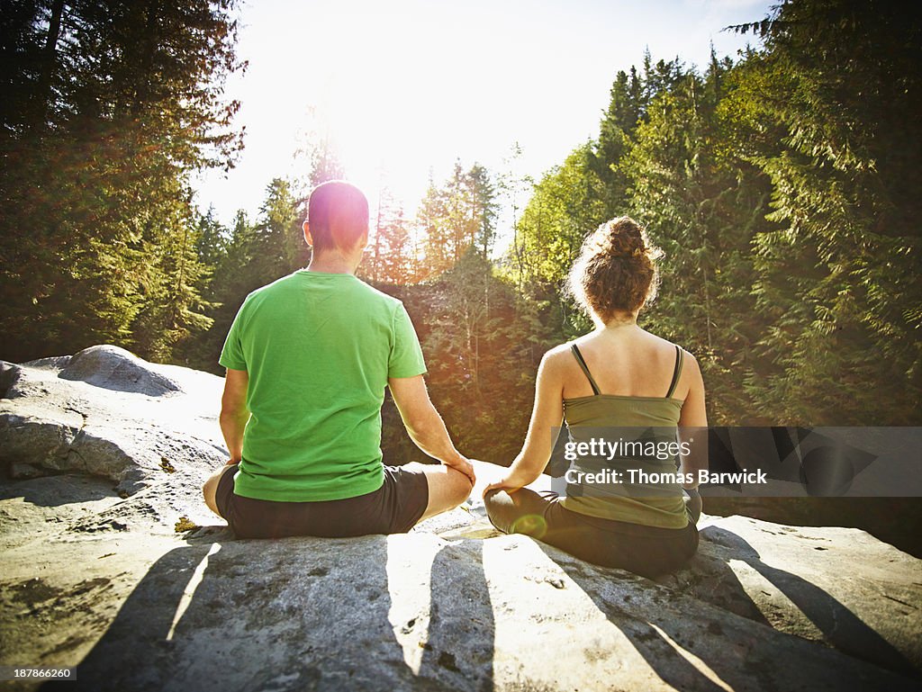 Couple meditating on rock in forest