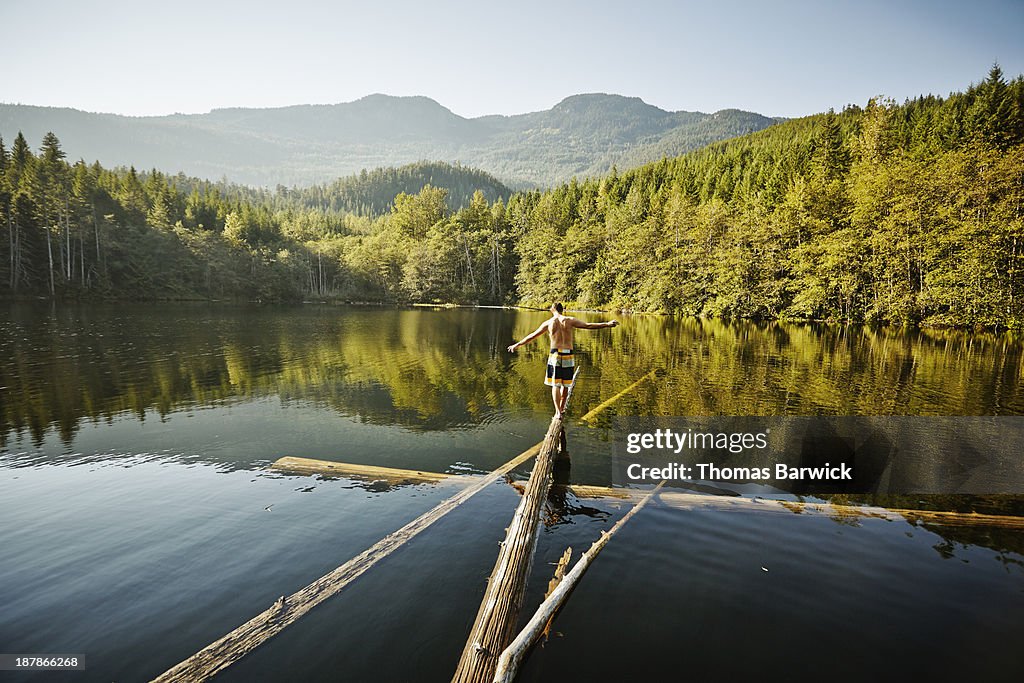 Man walking on log in alpine lake