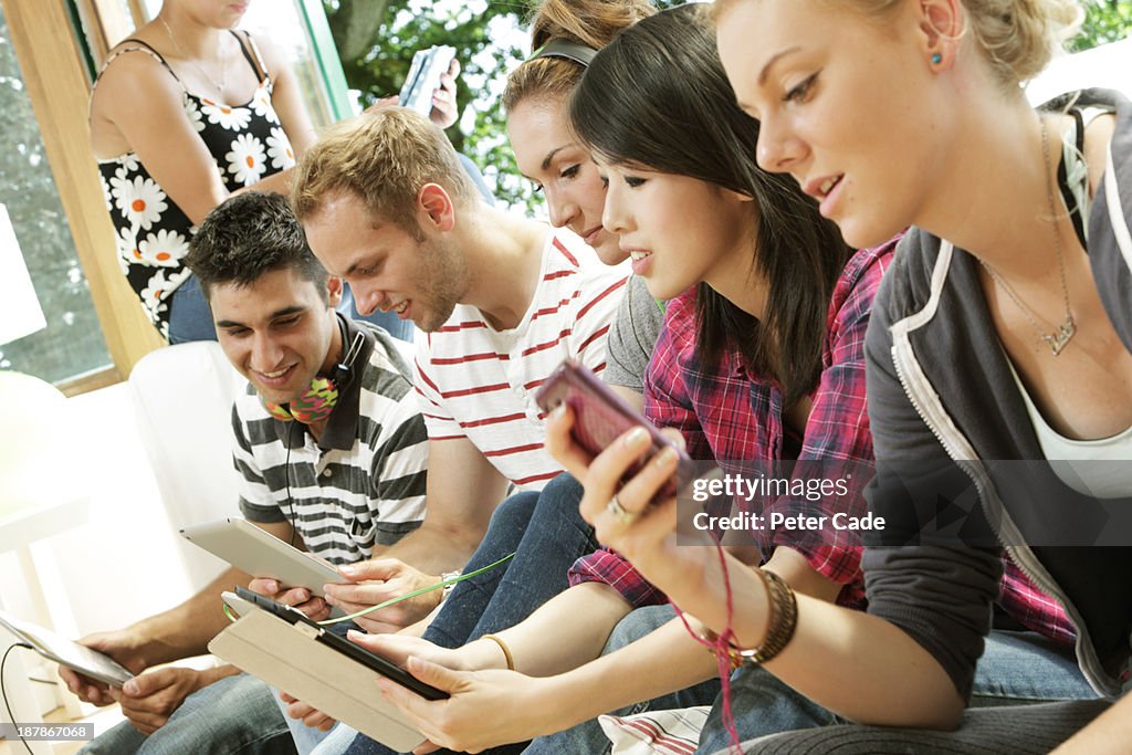 Teenagers on sofa looking at phones and tablets