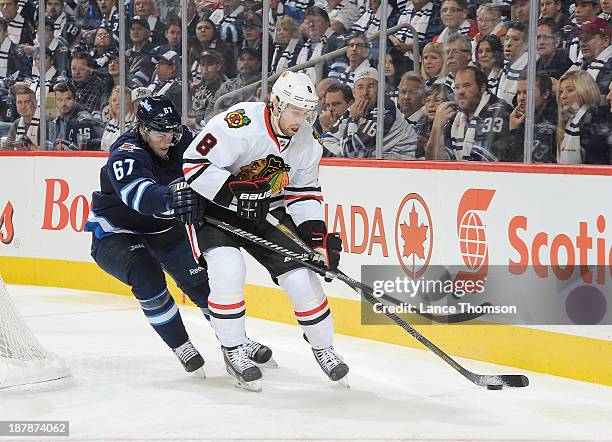 Nick Leddy of the Chicago Blackhawks plays the puck along the boards as Michael Frolik of the Winnipeg Jets battles from behind at the MTS Centre on...