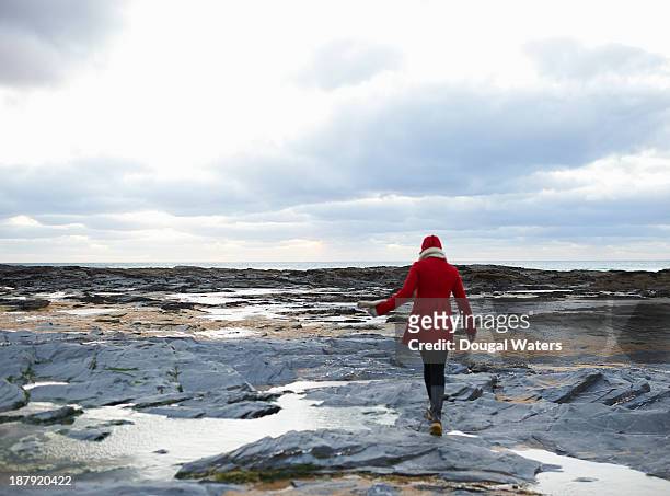 woman walking on rocky coastline. - winterjacke stock-fotos und bilder