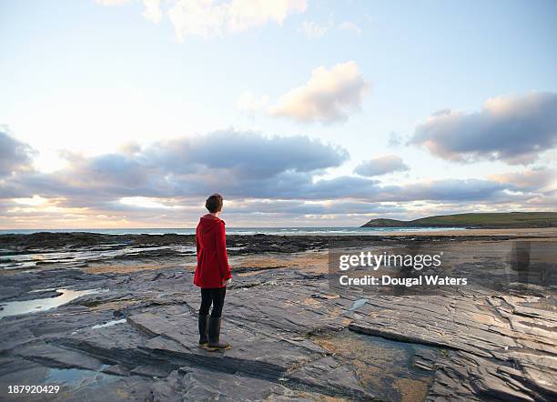 woman in red coat looking along coastline. - roter mantel stock-fotos und bilder